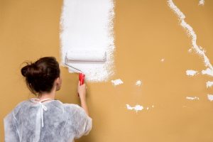 Frau streicht eine braune Wand weiß