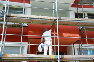 Maler steht auf einem Gerüst und streicht die Hausfassade